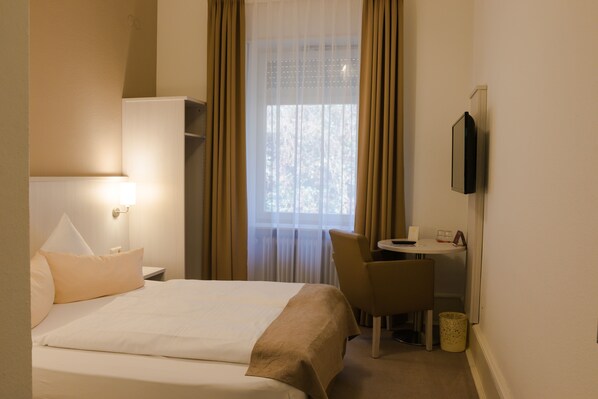 Habitación de hotel con cama, escritorio, silla, televisor y ventana con cortinas.