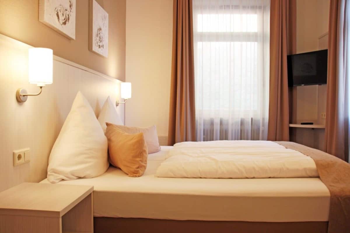 A hotel room with a bed, bedside lamps, a television, and artwork on the wall.