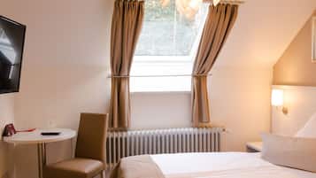 Habitación de hotel con cama, una silla, una mesa con control remoto y una ventana con cortinas.