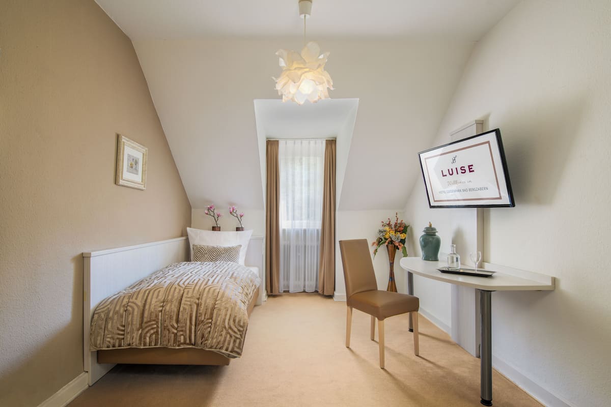 A bedroom with a bed, a chair, a desk, a TV, and a chandelier.