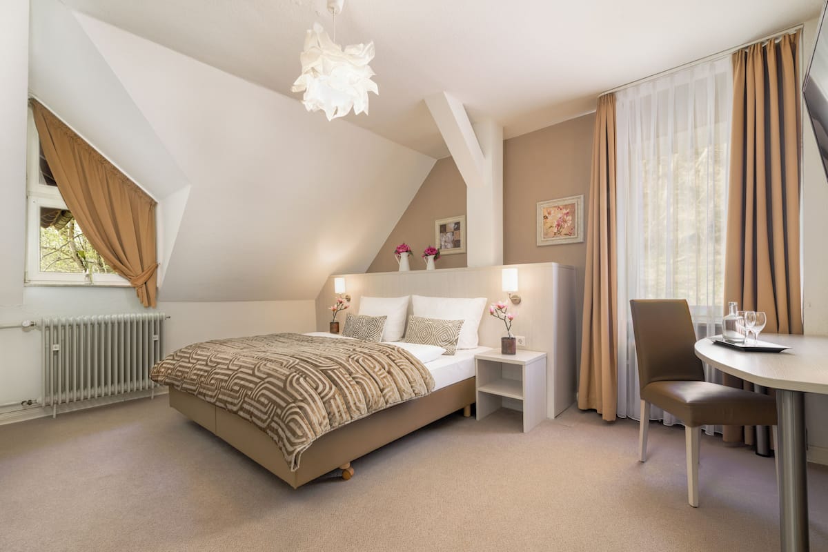 A bedroom with a bed, bedside tables, a chair, a table, and a window with curtains.