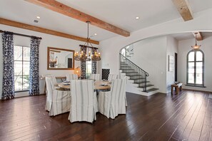 Une salle à manger spacieuse, avec une table et des chaises en bois, un lustre et un escalier menant à un autre niveau.