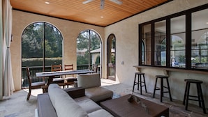 A spacious patio with a wooden ceiling, large arched windows, a dining table, and seating areas.