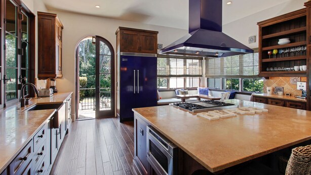 A modern kitchen with a central island, built-in appliances, and a view through a glass door.