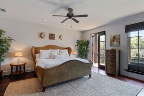 Une chambre avec un grand lit, un ventilateur de plafond, une fenêtre donnant sur un beau paysage et une porte menant à l’extérieur.