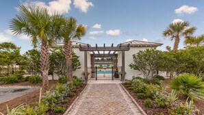 A gated entrance with a stone pathway leading to a pool area, surrounded by palm trees and flowering plants. - 601 Mariners Circle by Hodnett Cooper (St. Simons Island)