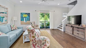 A living room with a sofa, chairs, a TV, and a staircase. - 601 Mariners Circle by Hodnett Cooper (St. Simons Island)