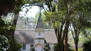 Une église blanche, dotée d’un clocher, entourée d’arbres et d’une pelouse bien entretenue.