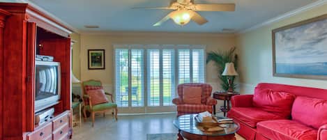 A living room with a red sofa, a wooden entertainment center, a glass coffee table, and a ceiling fan.