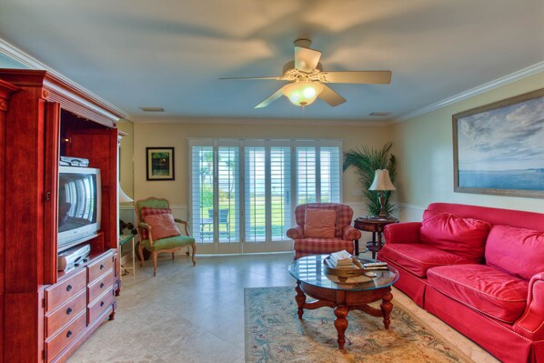 A living room with a red sofa, a wooden entertainment center, a glass coffee table, and a ceiling fan.