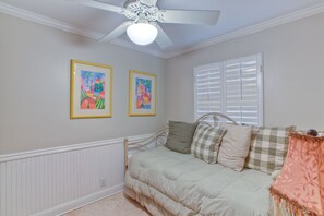 A bedroom with a bed, a ceiling fan, and two framed artworks on the wall.