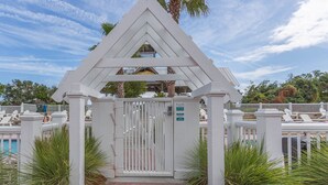 A gated entrance with a white pergola structure, a brick pathway, and a pool area with lounge chairs. - 22 Coast Cottages by Hodnett Cooper (St. Simons Island)