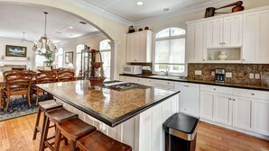 A spacious kitchen with a large island, white cabinetry, and a granite countertop. - 2225 Bruce Drive by Hodnett Cooper (St. Simons Island)