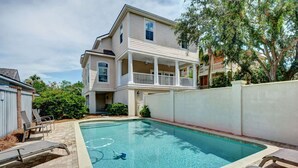 A residential swimming pool with lounge chairs, a covered patio, and a two-story house with a balcony. - 2225 Bruce Drive by Hodnett Cooper (St. Simons Island)