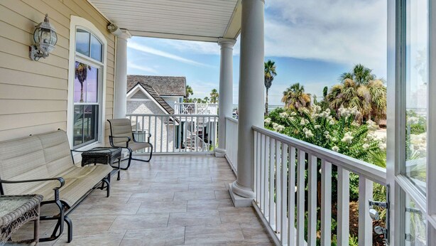A covered porch with a bench and chairs, a view of a house with a staircase, and a garden with cacti and palm trees. - 2225 Bruce Drive by Hodnett Cooper (St. Simons Island)