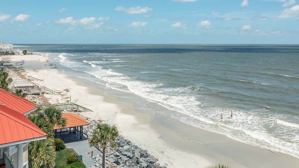 A beach view with a building featuring a red roof and a gazebo.