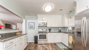 A kitchen with white cabinets, a stainless steel refrigerator, a microwave, an oven, and a tiled backsplash.