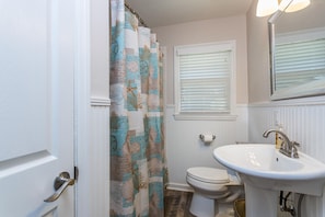 A bathroom with a toilet, sink, and shower curtain. - 647 Demere Way by Hodnett Cooper (St. Simons Island)