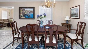 A dining room with a round table, six wooden chairs, a chandelier, and two framed paintings on the walls. - 11908 Old Demere Rd by Hodnett Cooper (St. Simons Island)