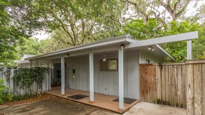 A covered porch with a wooden deck, a wooden fence, and a house with a white exterior. - 11908 Old Demere Rd by Hodnett Cooper (St. Simons Island)
