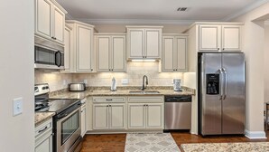 A modern kitchen with white cabinetry, stainless steel appliances, and a granite countertop. - 1203 Reserve Lane by Hodnett Cooper (St. Simons Island)