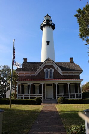 A lighthouse with a brick base and a white tower, a flagpole with an American flag, and a well-maintained lawn.