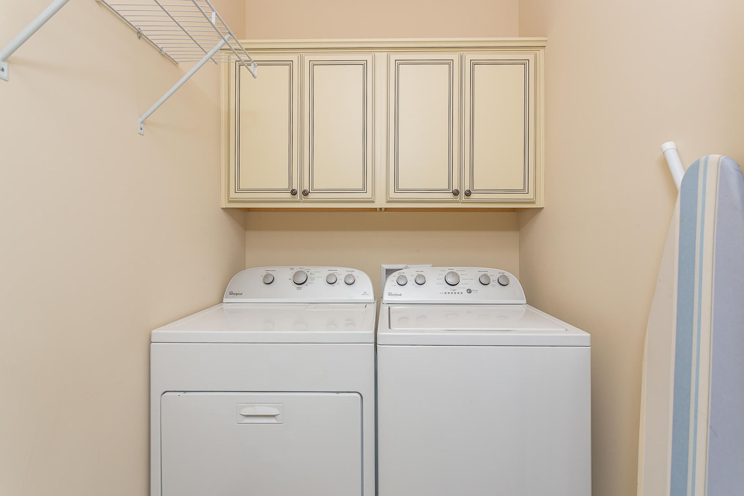 A laundry room with two stacked washers and dryers, a metal drying rack, and a striped towel hanging on the wall.