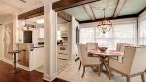 A dining area with a round table and four chairs, a kitchen in the background, and a wooden ceiling.