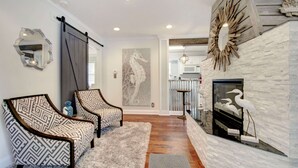 A modern living room with two patterned chairs, a fireplace with decorative birds, and a large mirror on the wall.