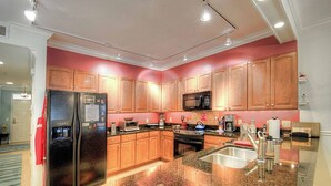 A modern kitchen with granite countertops, stainless steel appliances, wooden cabinets, and a central island with a sink. - 760 Ocean Boulevard #404 by Hodnett Cooper (St. Simons Island)