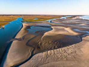 An aerial view of a coastal landscape with a river meandering through a sandy area, surrounded by fields and a distant shoreline.