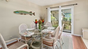 A dining area with a glass table surrounded by wicker chairs, a decorative fish wall hanging, and a view through a sliding glass door. - 111 Mews Circle by Hodnett Cooper (St. Simons Island)