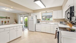 A modern kitchen with white cabinetry, a refrigerator, a dishwasher, and a microwave. There is a window providing natural light and a view of the outdoors. - 111 Mews Circle by Hodnett Cooper (St. Simons Island)