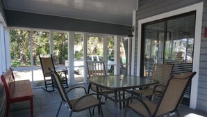 Een overdekt terras met een glazen tafel en stoelen, een rode bank en uitzicht op de straat en bomen.
