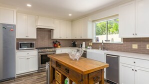 A modern kitchen with white cabinets, a wooden island, stainless steel appliances, and a window providing natural light. - 4316 7th Street by Hodnett Cooper (St. Simons Island)
