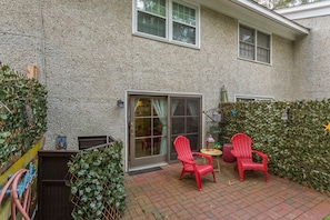 A patio with two red chairs and a small table, a sliding glass door, and a brick floor.
