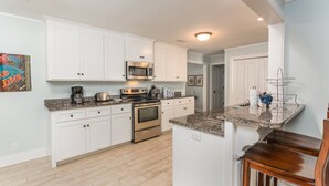 Una cocina moderna con armarios blancos, electrodomésticos de acero inoxidable, encimeras de granito y una zona de bar con taburetes.