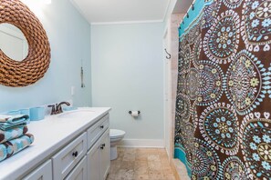 A bathroom with a white sink, a mirror, a toilet, and a patterned shower curtain.
