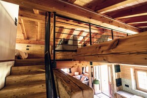 A wooden interior with a staircase, a bunk bed, and a window with curtains.