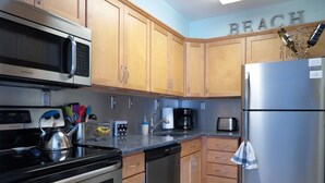 Una cocina con armarios de madera, un refrigerador de acero inoxidable, un microondas, una tetera y un tostador.
