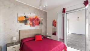 Ein modernes Schlafzimmer mit einem großen Bett, einem Nachttisch, einem Beistelltisch und einer Glastür, die auf einen Balkon führt.
