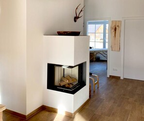 A modern interior with a fireplace, wooden flooring, and a dining area visible in the background.
