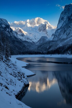 A serene mountain lake with snow-covered peaks and a clear sky. - Q6 Gosaubach - Apartment for up to 4 guests (Gosau)