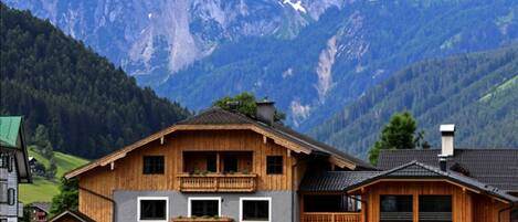 A wooden chalet with a balcony, a sign reading "DACHSTEIN", and a mountain backdrop.