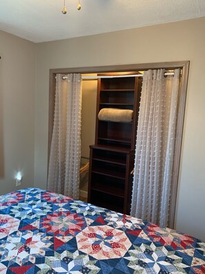 Une chambre à coucher avec un lit recouvert d’une courtepointe, une armoire contenant une serviette et une porte ornée de rideaux.