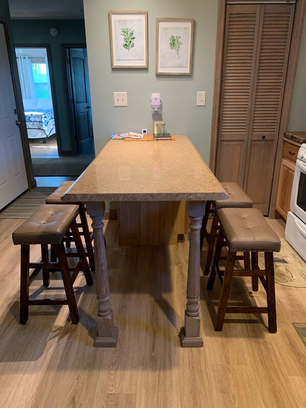 A wooden dining table with four stools, a kitchen area with wooden cabinets, and two framed botanical prints on the wall. - Cozy Modern Carriage Apartment Close to Shopping, Skiing,Golf (Petoskey)
