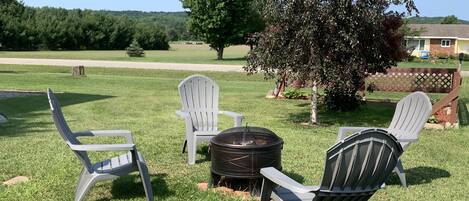 A grassy outdoor area with Adirondack chairs and a fire pit.
