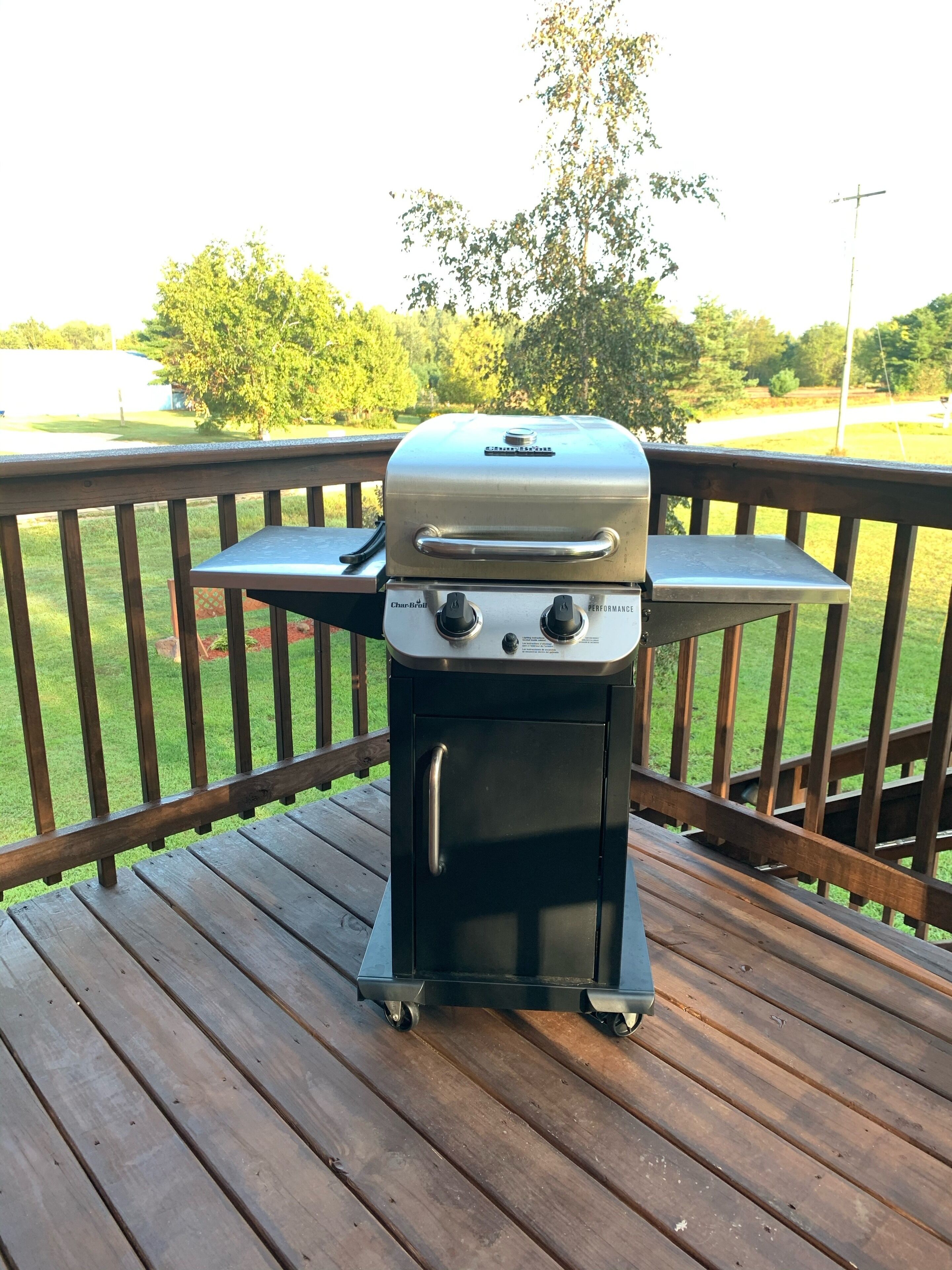 Una parrilla de gas Char-Broil sobre un muelle de madera, con un jardín césped y árboles al fondo.