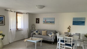 Una sala de estar acogedora con un sofá, una mesa de comedor con sillas, una lámpara y un cuadro de un faro.
