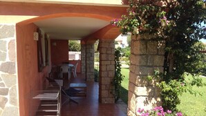 Un porche cubierto al aire libre con pared de piedra, un tendedero de metal y una mesa con sillas.